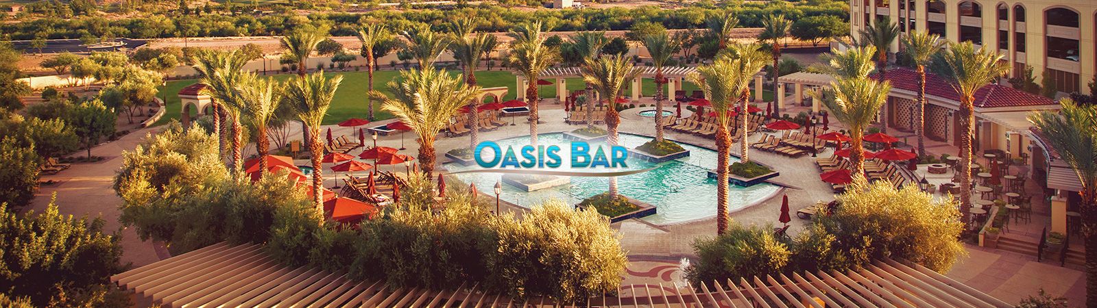 Aerial view of a hotel pool area with lounge chairs, umbrellas, and palm trees, with a bar in the background.
