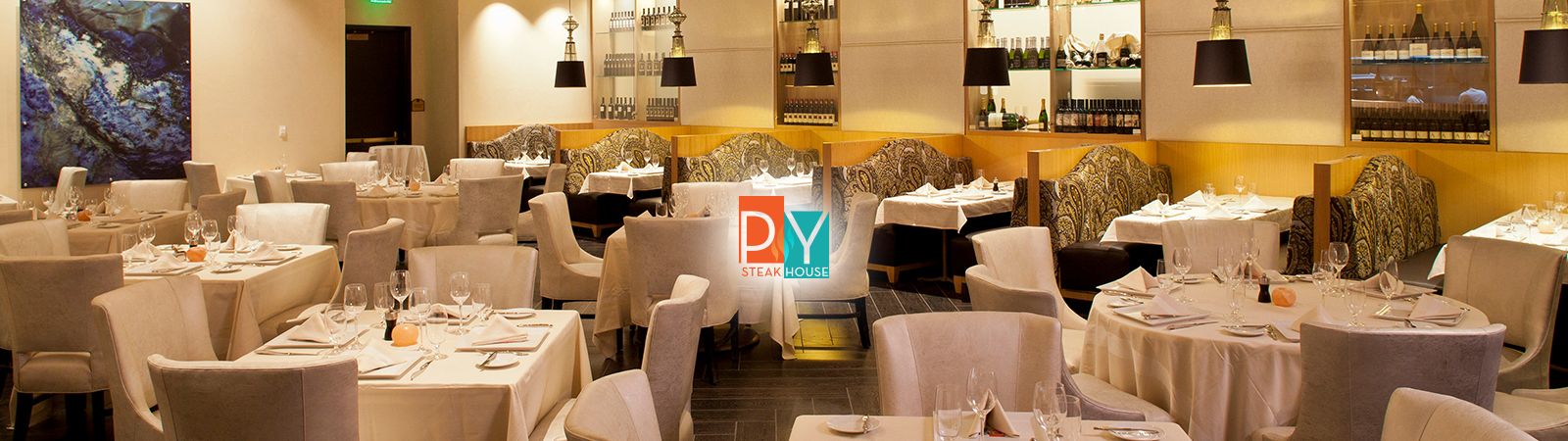 A dining room with multiple tables set for dinner, white tablecloths, and a bar in the background.